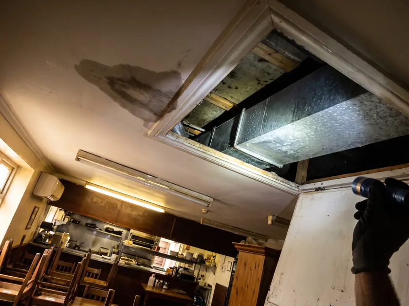 Condensation droplets on an uninsulated duct and a damp stain on a restaurant ceiling