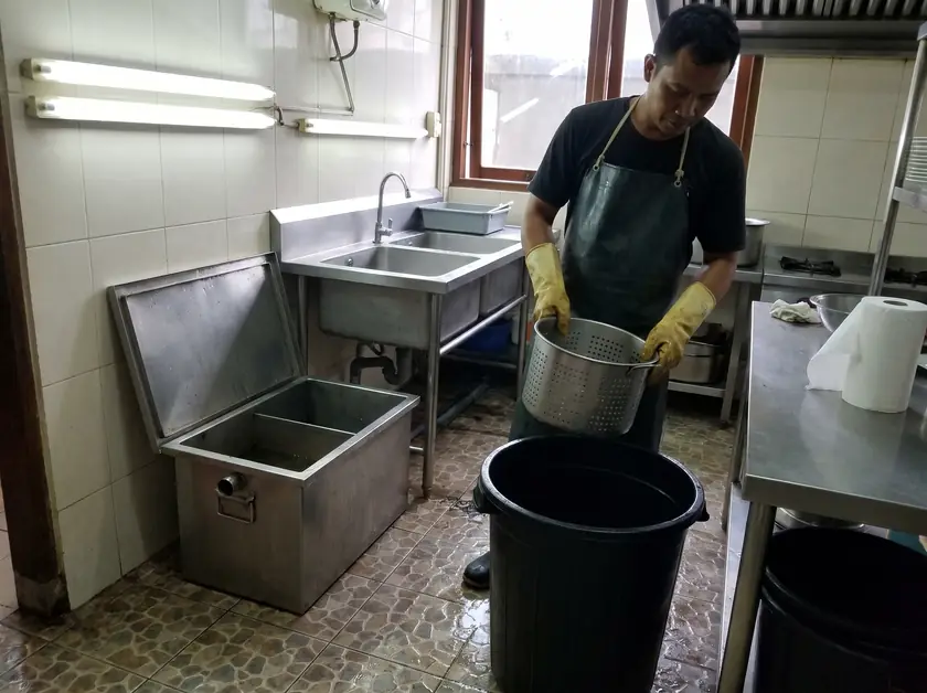 Technician cleaning the basket of a stainless grease trap under a kitchen sink
