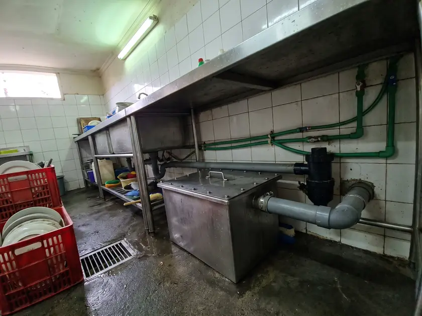 Stainless grease trap and drainage pipework under a scullery sink in a Jimbaran restaurant