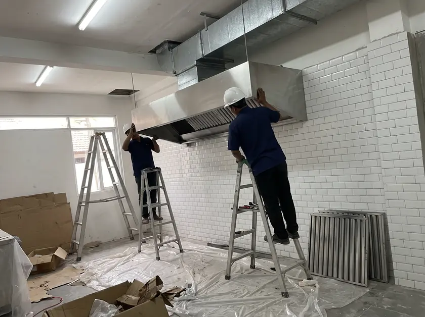 Technicians installing a stainless canopy hood and galvanized exhaust duct in a Seminyak restaurant kitchen